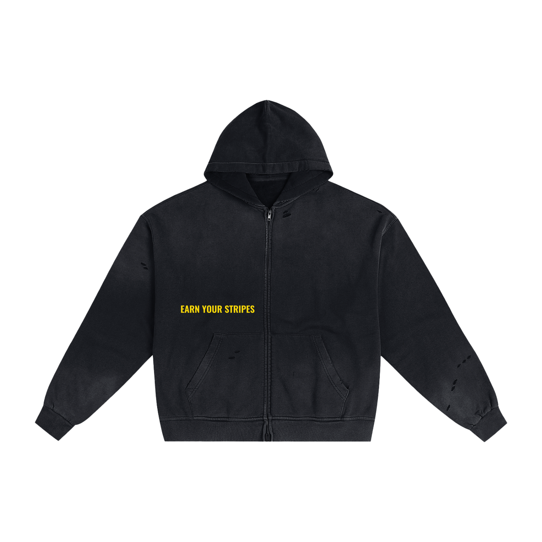 A black distressed zip-up hoodie with yellow text reading 'EARN YOUR STRIPES' on the left chest, displayed on a solid white background.