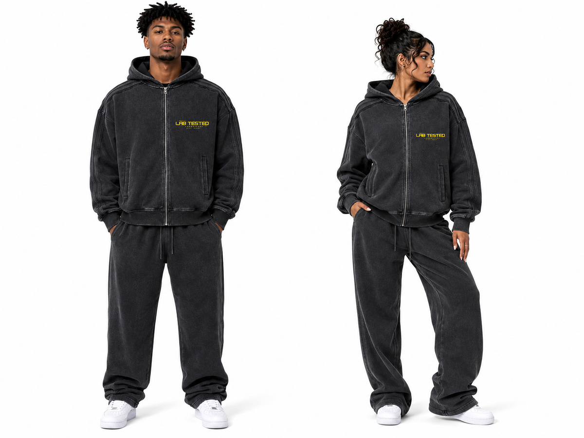 Two models wearing a matching black washed zip-up hoodie and sweatpants set with yellow 'LAB TESTED' text on the chest, shown against a plain white background.
