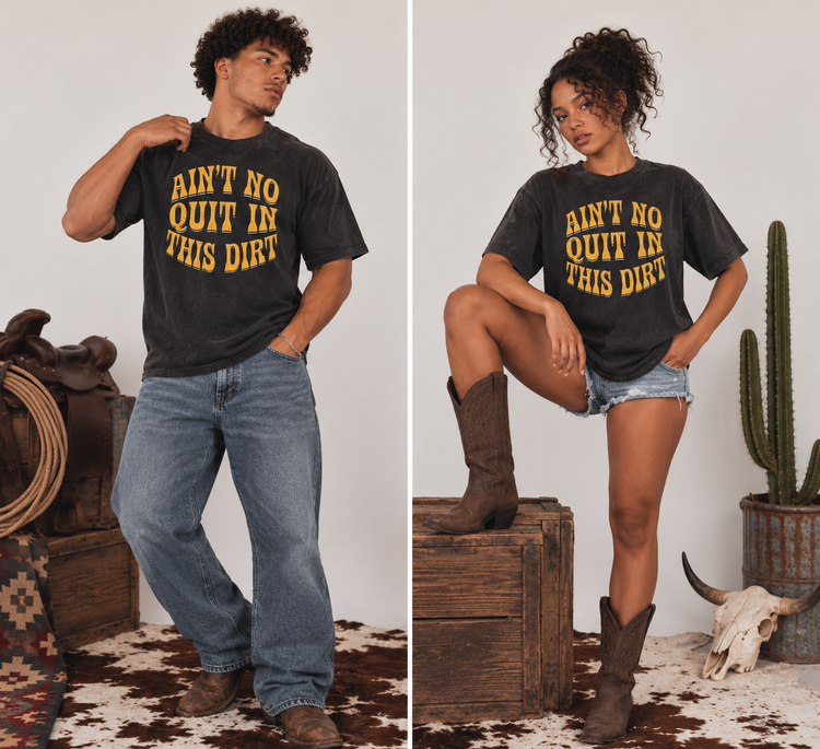 A split-screen lifestyle image showing a man and a woman modeling a black graphic t-shirt with yellow text that reads 'AIN'T NO QUIT IN THIS DIRT'. The man wears blue jeans and brown boots, while the woman wears denim shorts and brown boots, set against a rustic western-themed backdrop with a cowhide rug, wooden crates, a cactus, and a skull.