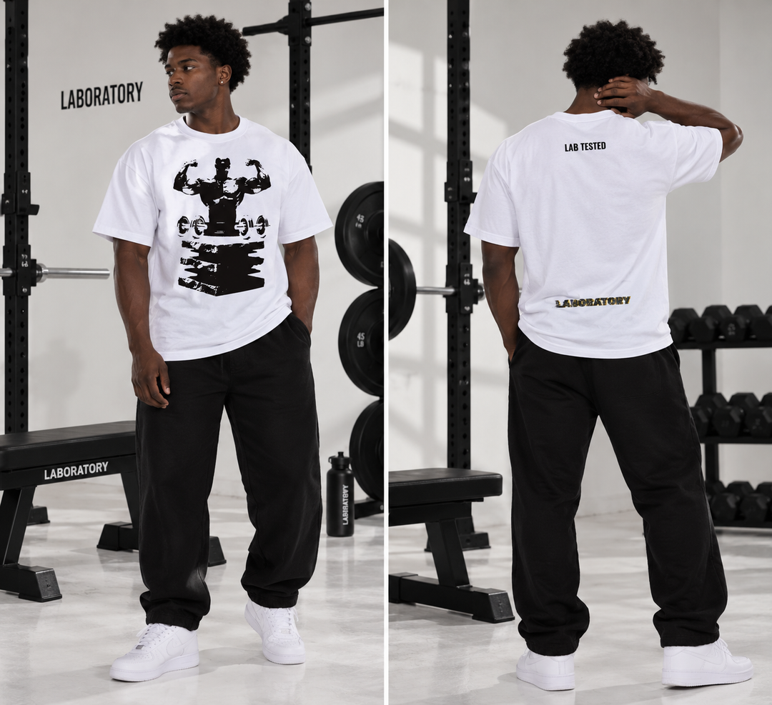 A man modeling a white short-sleeve t-shirt with a black graphic print on the front and 'LABORATORY' branding on the back, paired with black sweatpants and white sneakers in a gym setting.
