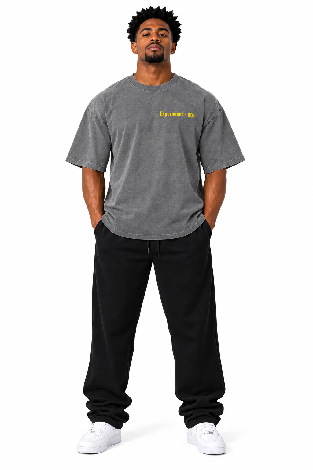 A man modeling a heather gray t-shirt with yellow 'Experiment-001' text on the chest, paired with black sweatpants and white sneakers, against a plain white background.