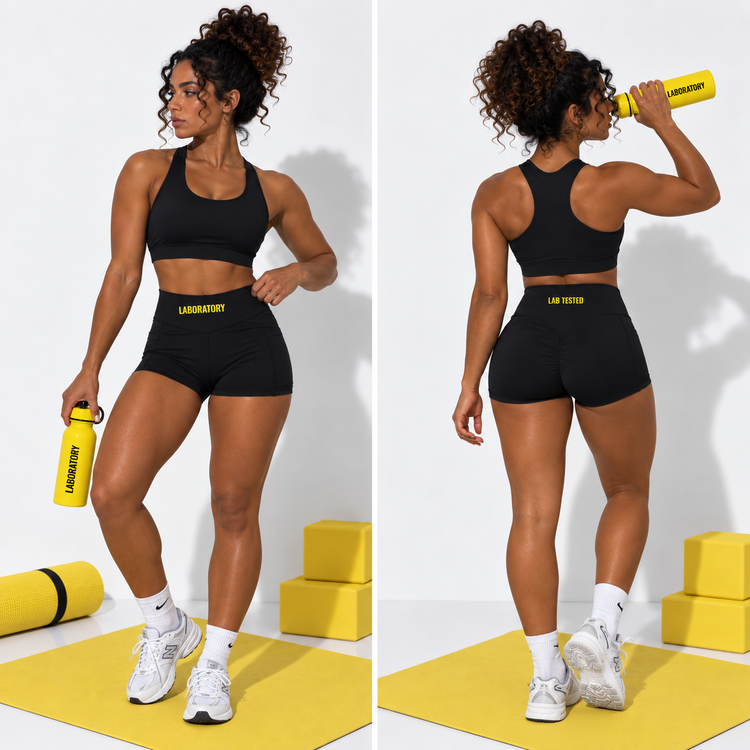 A side-by-side studio photo of a woman modeling black athletic shorts and a matching black sports bra with yellow 'LAB TEST' branding. She is shown from the front and back, holding a yellow LAB TEST water bottle, on a white background with yellow exercise blocks and a yellow mat.