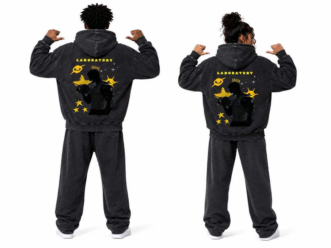 Two models shown from the back wearing matching washed black hoodies and sweatpants sets with a large yellow and black graphic on the back reading LABORATORY.