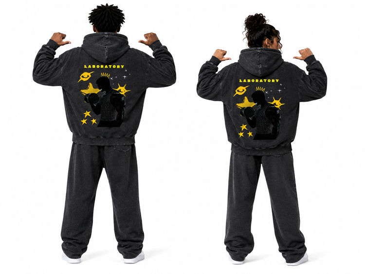 Two models shown from the back wearing matching washed black hoodies and sweatpants sets with a large yellow and black graphic on the back reading LABORATORY.