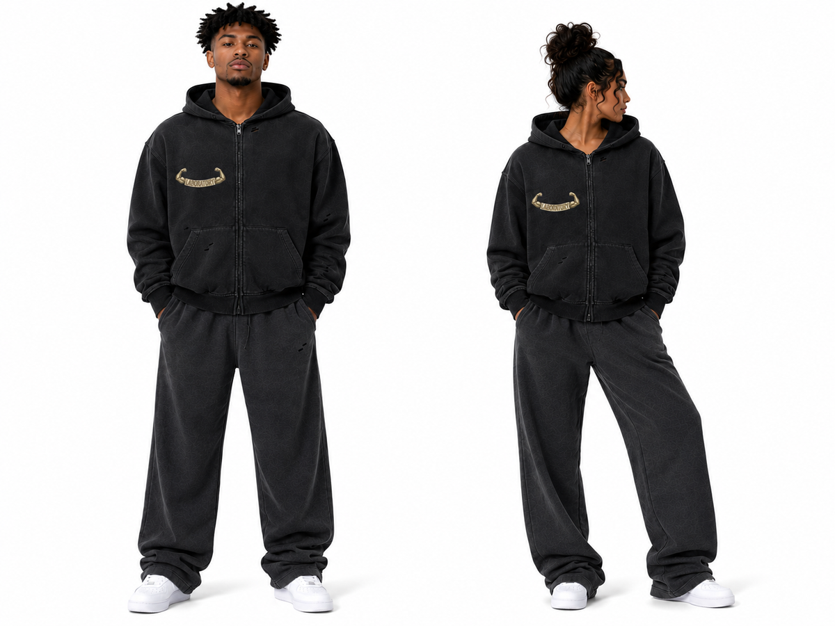 A man modeling a black zip-up hoodie and matching sweatpants set, shown from the front and side against a plain white background. The hoodie features a small gold graphic on the left chest.