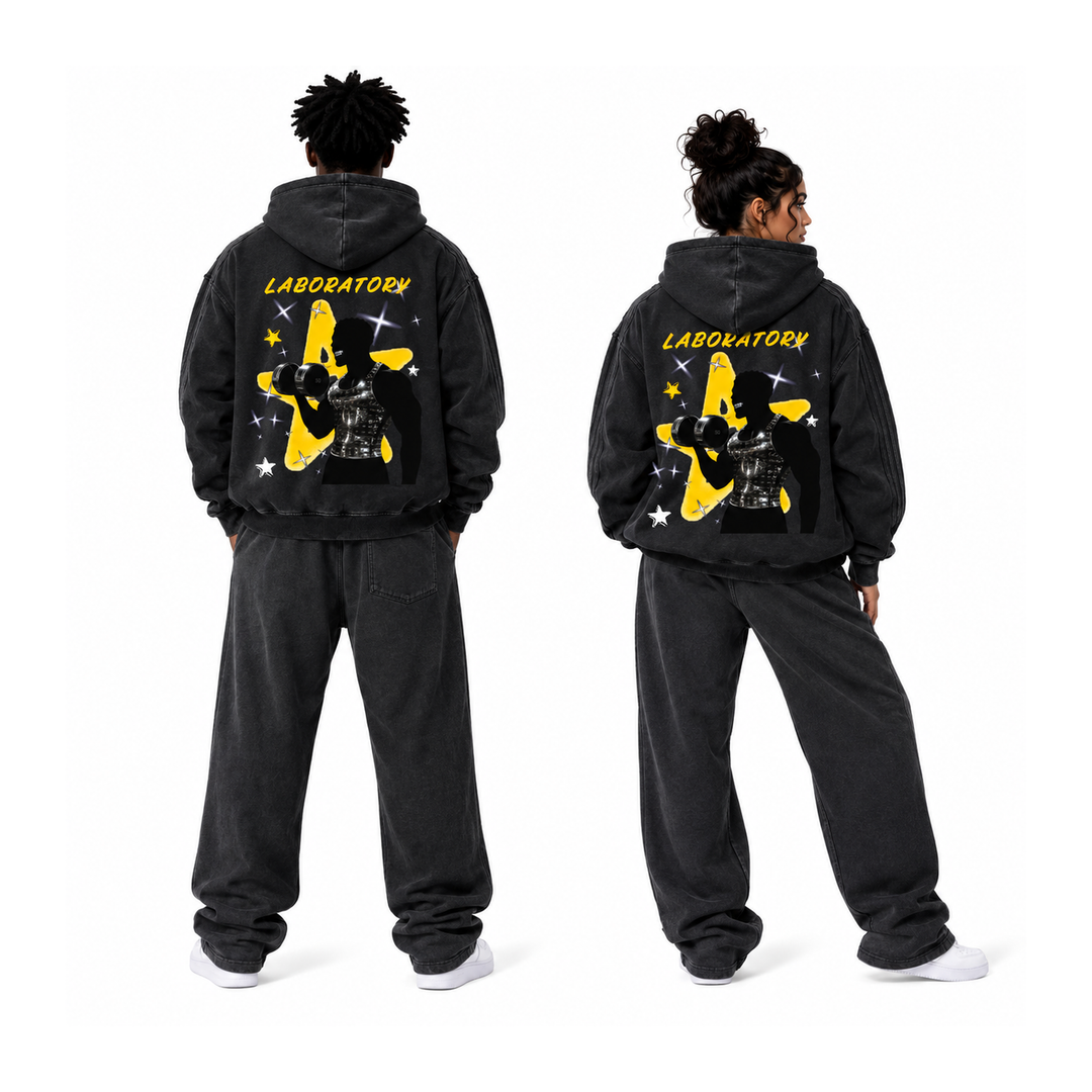 Two models shown from the back wearing matching washed black hoodies and sweatpants sets, featuring a large yellow and black graphic with the word 'LABORATORY' on the back, against a plain white background.
