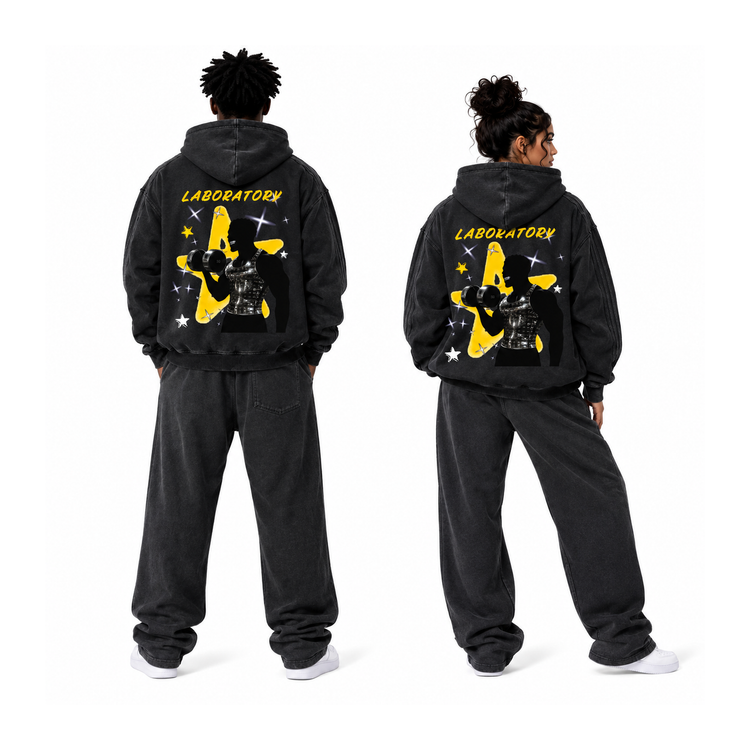 Two models shown from the back wearing matching washed black hoodies and sweatpants sets, featuring a large yellow and black graphic with the word 'LABORATORY' on the back, against a plain white background.